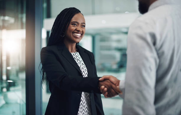 A black woman in a black suit, giving a black man a handshake.