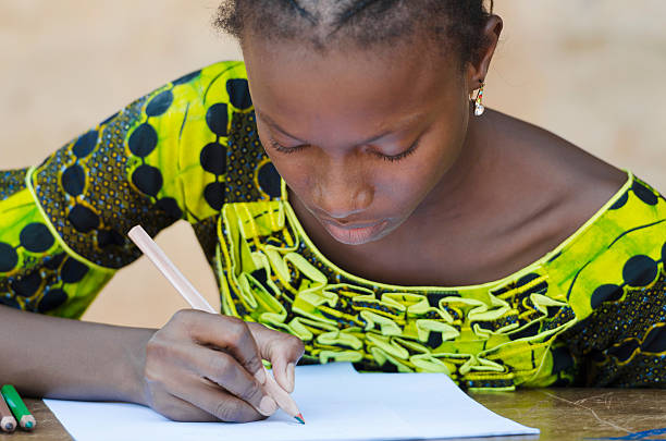 Close-Up shot of a gorgeous black girl writing on a piece of paper. She is wearing a yellow / green dress.