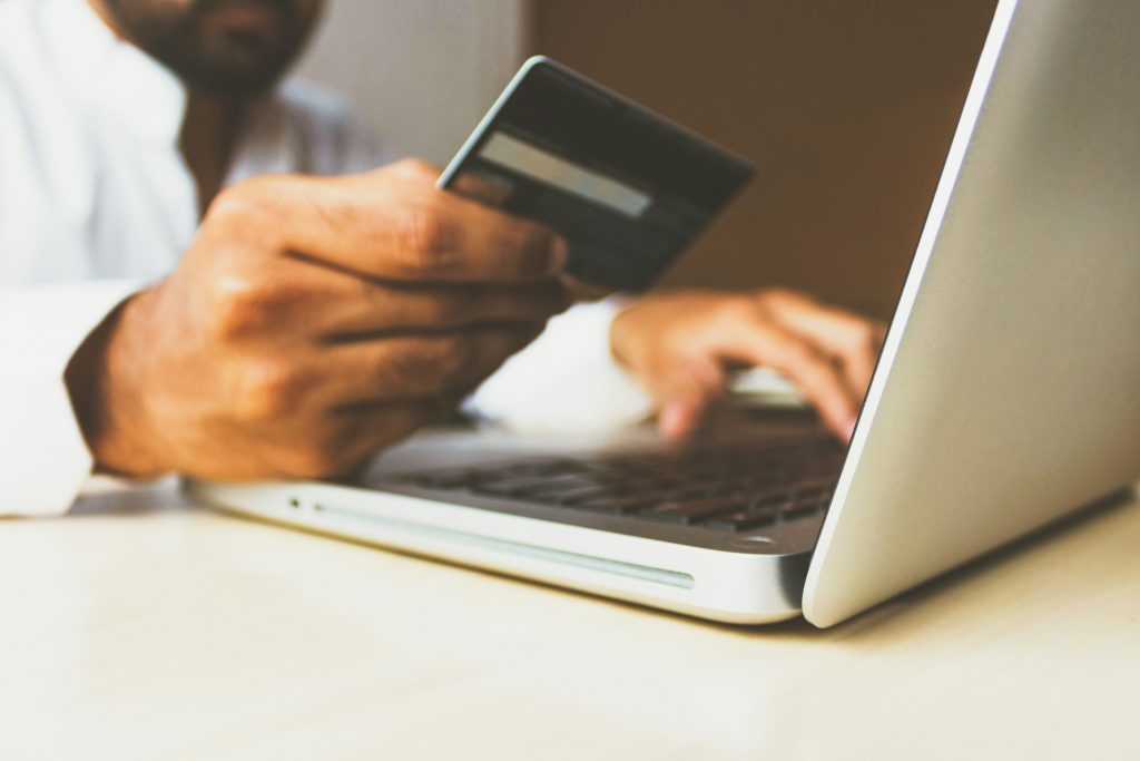 Close-up of a person's hands holding a credit card while typing on a laptop, indicating an online transaction or shopping activity.